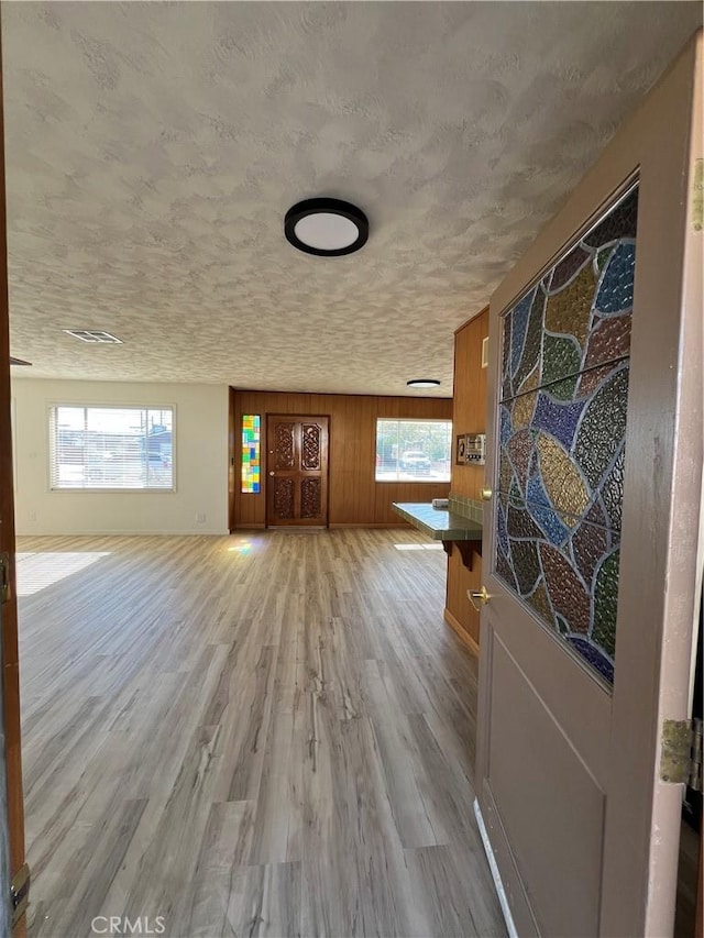 unfurnished living room featuring wooden walls, a textured ceiling, visible vents, and wood finished floors