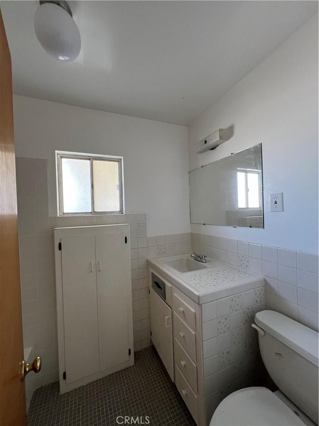 bathroom with toilet, wainscoting, tile walls, and vanity