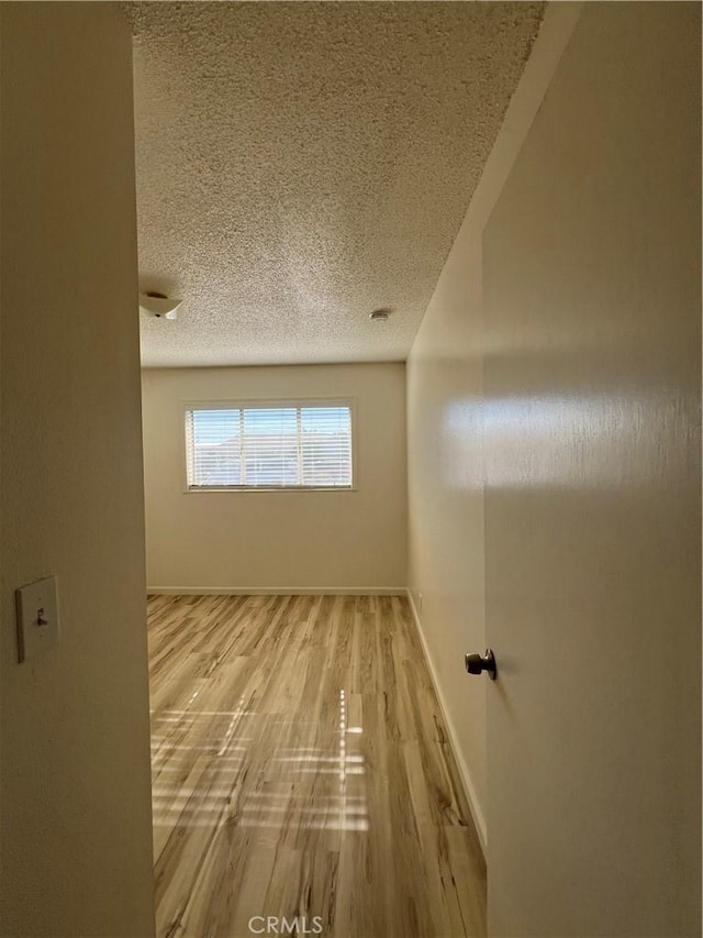 unfurnished room with light wood-type flooring, baseboards, and a textured ceiling