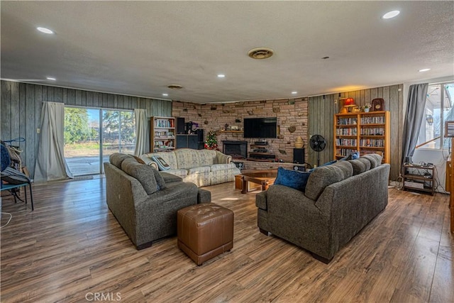 living room with wood-type flooring, a large fireplace, a textured ceiling, and wood walls