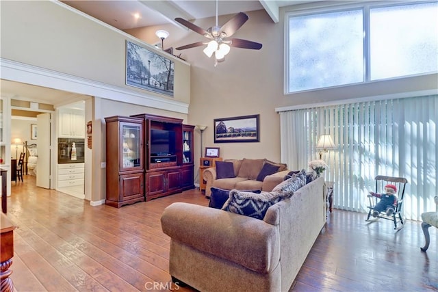 living room with wood-type flooring, a towering ceiling, ceiling fan, and beam ceiling