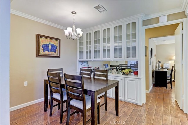 dining room featuring light wood-type flooring, ornamental molding, and an inviting chandelier