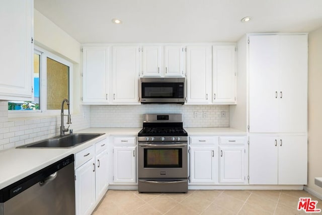 kitchen with appliances with stainless steel finishes, tasteful backsplash, sink, light tile patterned floors, and white cabinets