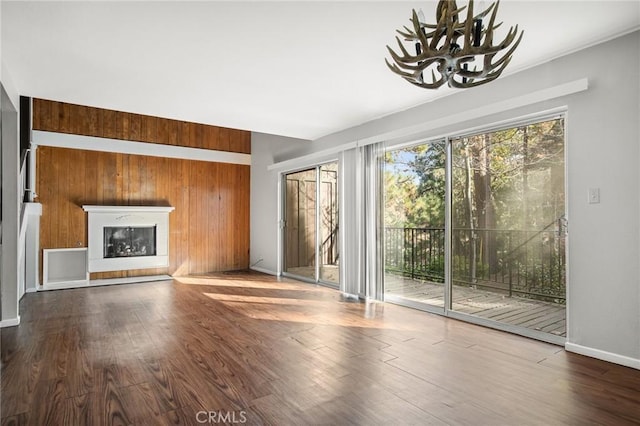 unfurnished living room featuring a chandelier, hardwood / wood-style floors, and wooden walls