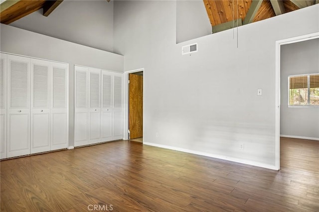 unfurnished bedroom with beam ceiling, multiple closets, hardwood / wood-style floors, and high vaulted ceiling