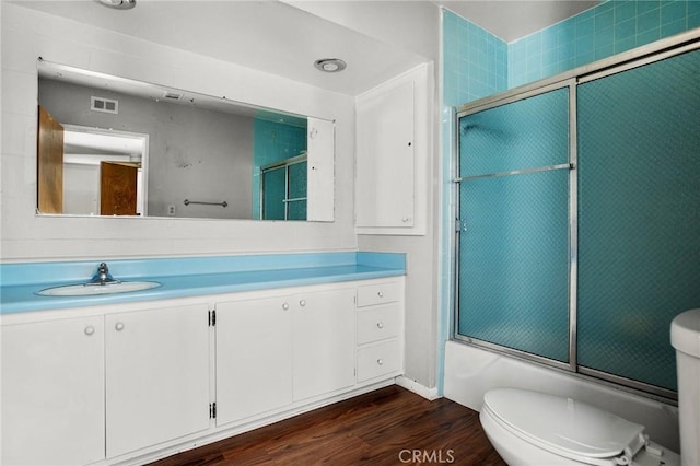 full bathroom featuring toilet, vanity, enclosed tub / shower combo, and hardwood / wood-style flooring