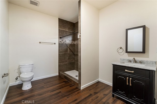 bathroom featuring tiled shower, vanity, wood-type flooring, and toilet