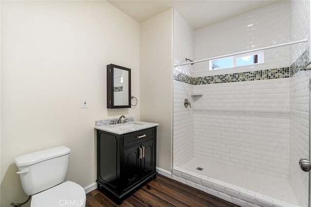 bathroom with hardwood / wood-style flooring, vanity, toilet, and tiled shower