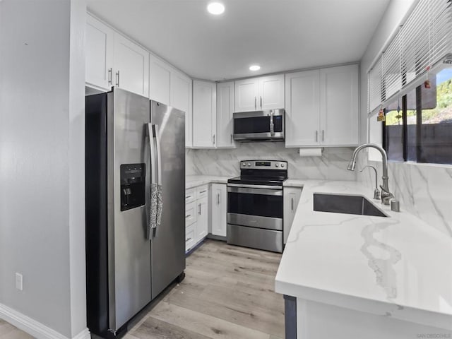 kitchen featuring appliances with stainless steel finishes, tasteful backsplash, sink, light hardwood / wood-style flooring, and white cabinets