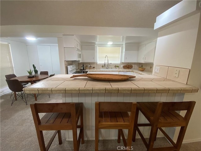 kitchen with kitchen peninsula, white appliances, white cabinetry, and a breakfast bar area