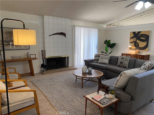 living room with a tile fireplace, ceiling fan, carpet, and a textured ceiling