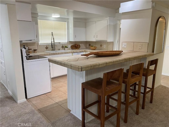 kitchen with a breakfast bar, kitchen peninsula, tile counters, washer / dryer, and white cabinetry