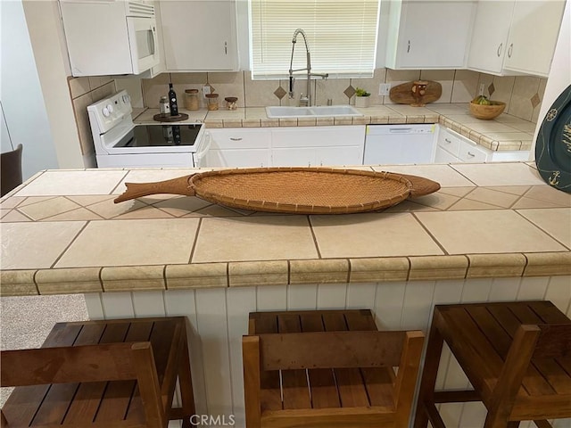 kitchen featuring white appliances, white cabinets, sink, decorative backsplash, and tile counters