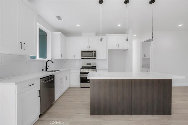 kitchen featuring white cabinets, pendant lighting, a kitchen island, and stainless steel appliances