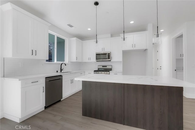 kitchen with white cabinetry, a kitchen island, decorative light fixtures, and appliances with stainless steel finishes