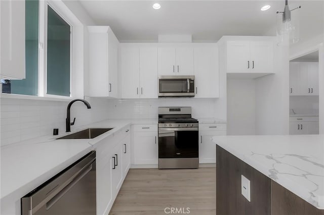 kitchen featuring appliances with stainless steel finishes, sink, pendant lighting, light hardwood / wood-style flooring, and white cabinets