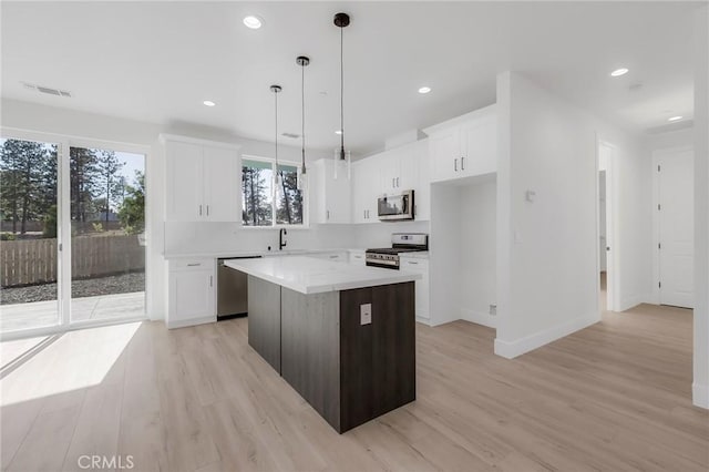 kitchen featuring a kitchen island, light hardwood / wood-style floors, decorative light fixtures, white cabinets, and appliances with stainless steel finishes