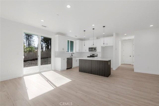 kitchen featuring a center island, appliances with stainless steel finishes, decorative light fixtures, light hardwood / wood-style floors, and white cabinetry