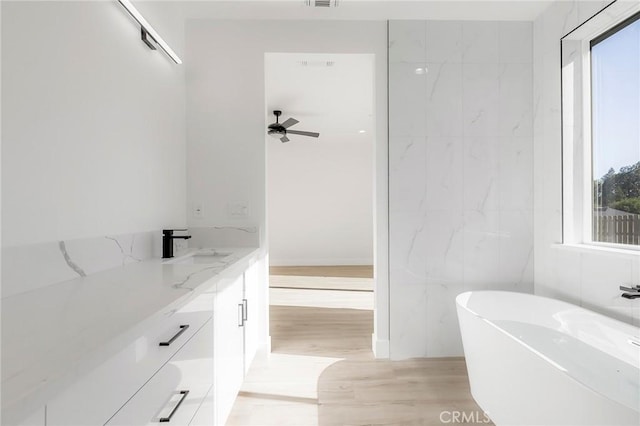 bathroom with a tub to relax in, ceiling fan, vanity, and wood-type flooring