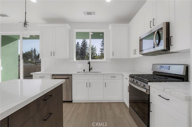 kitchen with stainless steel appliances, sink, light hardwood / wood-style flooring, white cabinetry, and hanging light fixtures