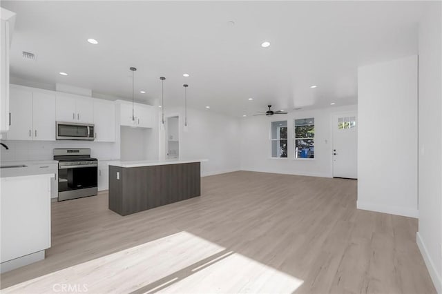 kitchen with white cabinetry, light hardwood / wood-style flooring, decorative light fixtures, a kitchen island, and appliances with stainless steel finishes