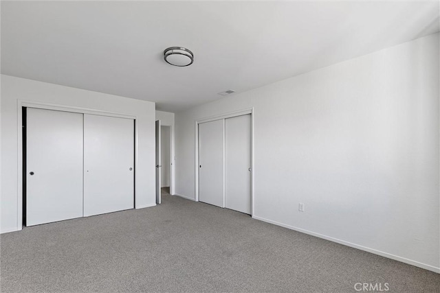 unfurnished bedroom featuring two closets and light carpet