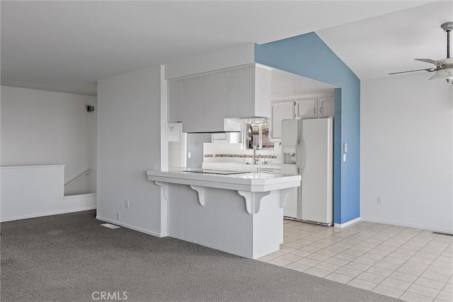 kitchen featuring vaulted ceiling, kitchen peninsula, light tile patterned flooring, white refrigerator with ice dispenser, and a breakfast bar area