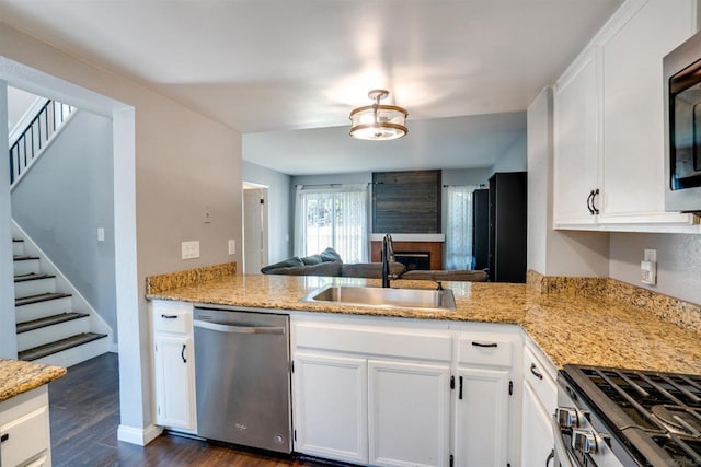 kitchen featuring a large fireplace, stainless steel appliances, dark wood-type flooring, sink, and white cabinets