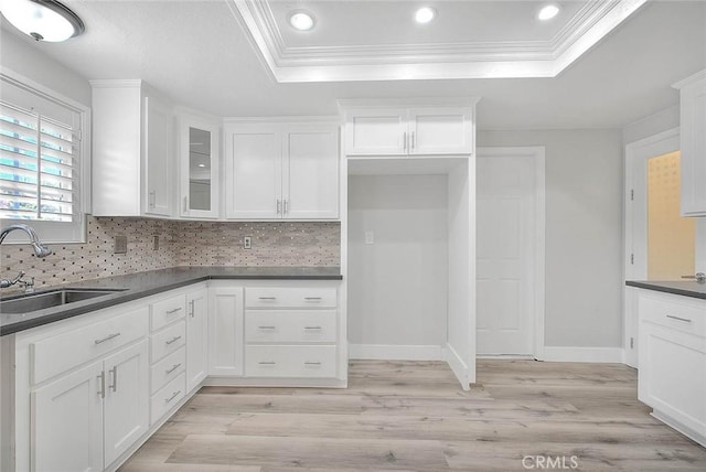 kitchen featuring white cabinetry, sink, light hardwood / wood-style flooring, decorative backsplash, and ornamental molding