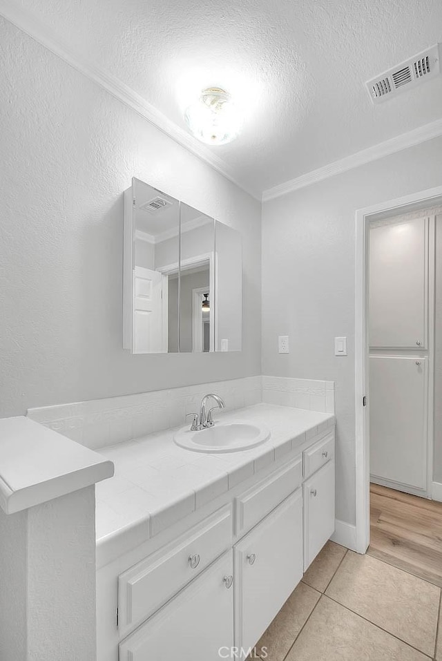 bathroom with tile patterned flooring, vanity, a textured ceiling, and ornamental molding