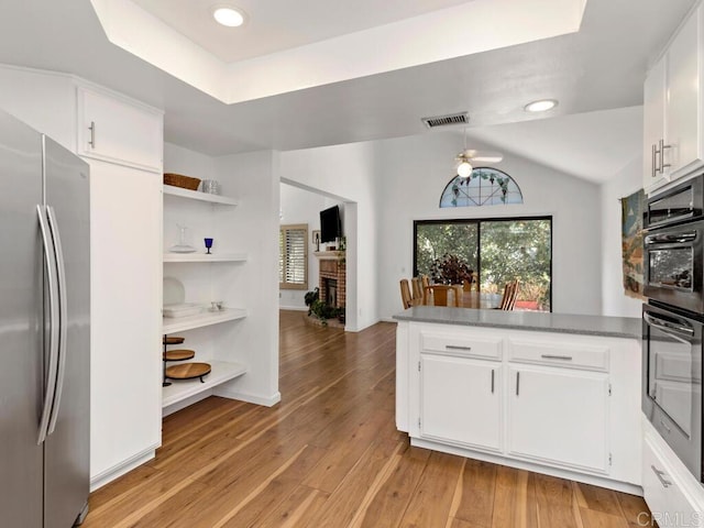 kitchen featuring white cabinets, stainless steel refrigerator, kitchen peninsula, light wood-type flooring, and multiple ovens