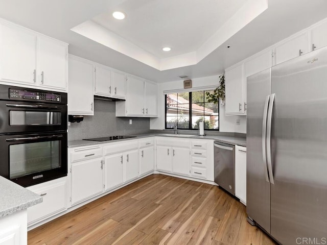 kitchen featuring white cabinetry, black appliances, a raised ceiling, and light wood-type flooring