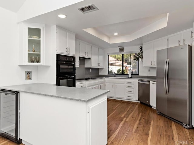 kitchen featuring black appliances, white cabinetry, kitchen peninsula, wine cooler, and a tray ceiling