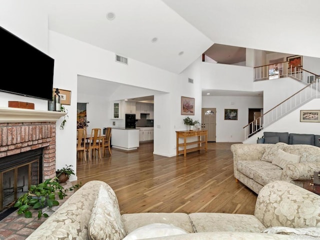 living room with hardwood / wood-style floors, high vaulted ceiling, and a brick fireplace