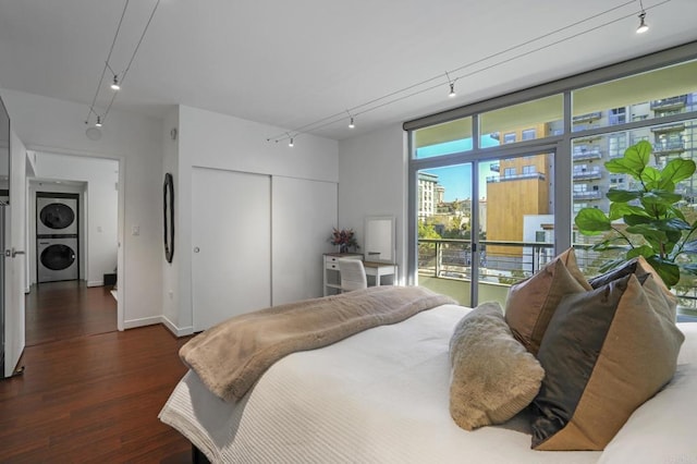 bedroom featuring a closet, stacked washing maching and dryer, dark wood-type flooring, and track lighting