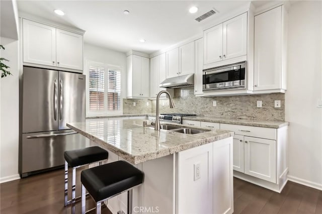 kitchen featuring white cabinets, light stone counters, an island with sink, dark hardwood / wood-style flooring, and stainless steel appliances