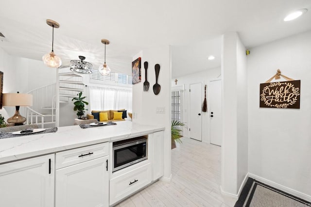 kitchen with light stone countertops, light wood-type flooring, pendant lighting, white cabinets, and stainless steel microwave