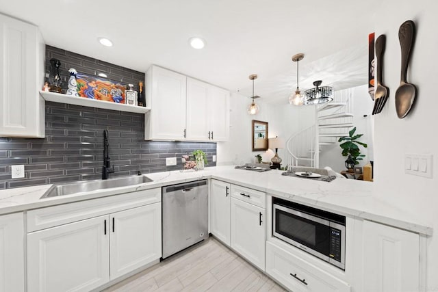 kitchen with kitchen peninsula, appliances with stainless steel finishes, light stone countertops, sink, and white cabinets