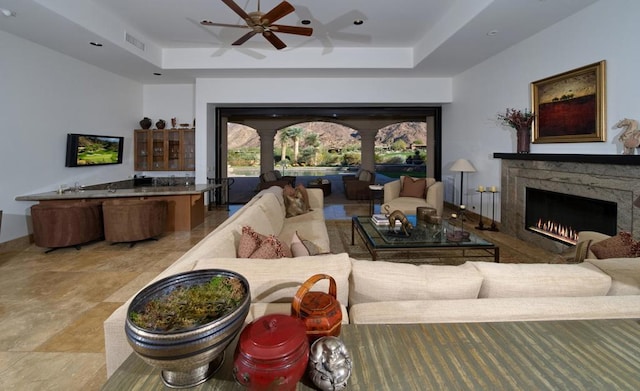 living room with a tray ceiling, ceiling fan, and a premium fireplace