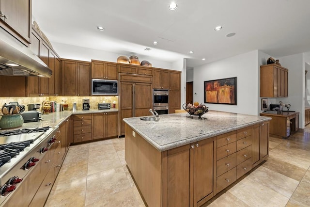 kitchen with backsplash, a center island with sink, sink, built in appliances, and light stone counters