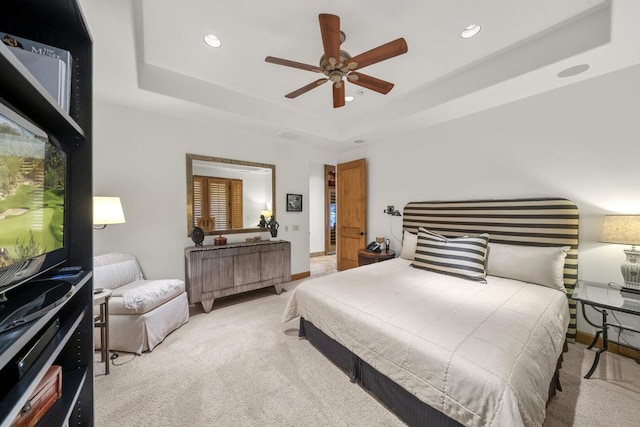 bedroom with ceiling fan, light colored carpet, and a tray ceiling