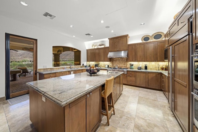 kitchen with a breakfast bar, a center island, sink, light stone countertops, and tasteful backsplash