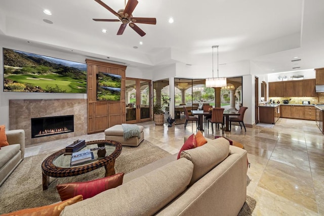 living room with ceiling fan with notable chandelier, a raised ceiling, and a high end fireplace