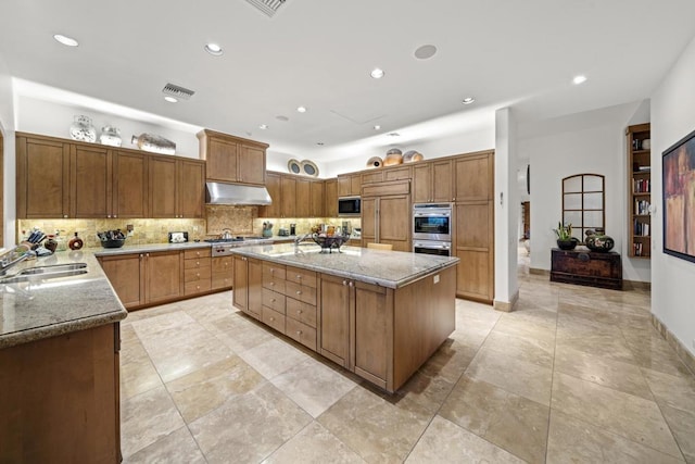 kitchen featuring a center island, backsplash, sink, built in appliances, and light stone countertops