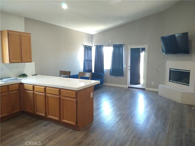 kitchen featuring lofted ceiling, dark hardwood / wood-style flooring, tile counters, kitchen peninsula, and a tiled fireplace