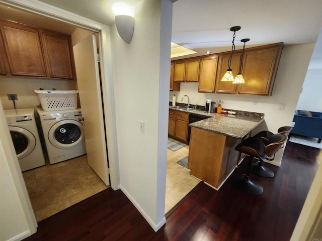 kitchen featuring hanging light fixtures, washing machine and dryer, a kitchen breakfast bar, black dishwasher, and dark hardwood / wood-style flooring