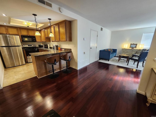 kitchen featuring a breakfast bar area, hanging light fixtures, dark stone countertops, appliances with stainless steel finishes, and kitchen peninsula