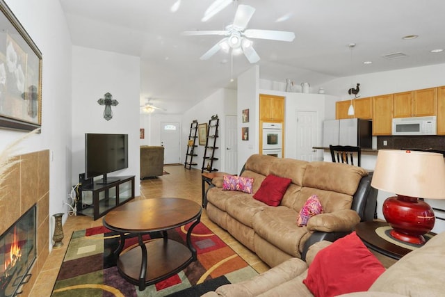 tiled living room featuring ceiling fan, lofted ceiling, and a tiled fireplace