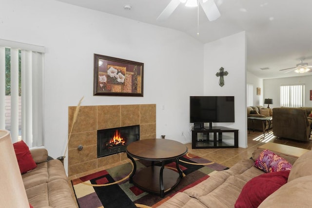 tiled living room featuring vaulted ceiling, ceiling fan, and a tiled fireplace