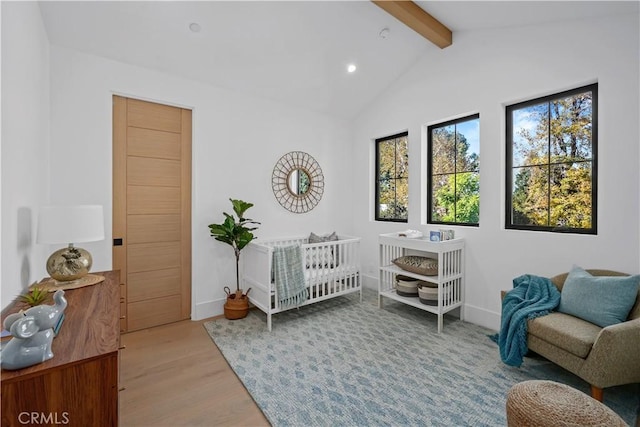 bedroom with light wood-type flooring, lofted ceiling with beams, and a nursery area